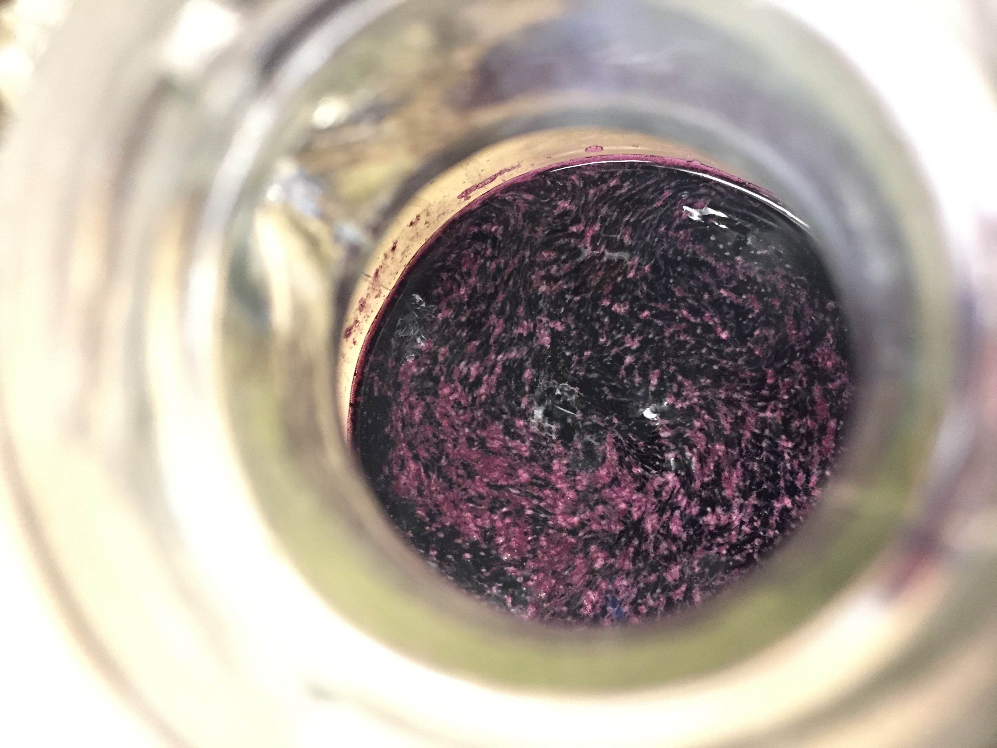 Looking into wine fermentation vessel. Red win infected with a layer of surface mold.